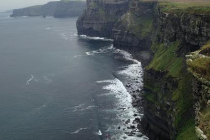 Cliffs with ocean waves below, under a cloudy sky. This alt text was added with Al; accuracy may vary.