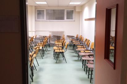 Classroom with rows of empty desks and chairs, viewed through an open door. This alt text was added with Al; accuracy may vary.