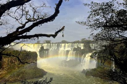 Waterfall framed by trees with a rainbow in the mist. This alt text was added with Al; accuracy may vary.