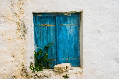 Weathered blue wooden door set in a white wall with some plants nearby. This alt text was added with Al; accuracy may vary.