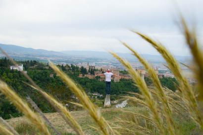 A hand framing a distant lighthouse with stone path along the water. This alt text was added with Al; accuracy may vary.