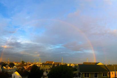 Full rainbow in blue sky with clouds over town