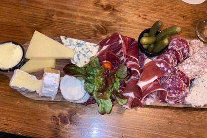 Charcuterie board with butter, various cheeses, meats, lettuce, and pickles sitting on a table.
