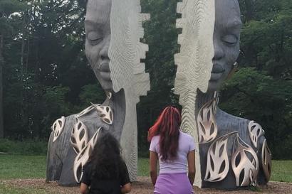My sister and I facing a sculpture of a head split in two.