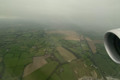 Thick fog hovers over a sea of green, viewed from the window of an airplane