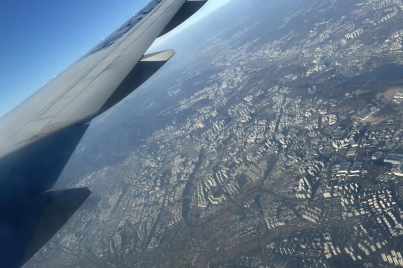 View outside of a plane window showing the Chicago metropolitan area, the right wing of a plane, and a blue sky.