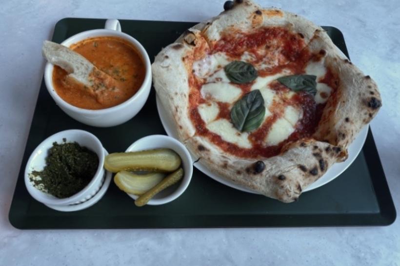 Pizza, tomato soup, and pickles on a tray.
