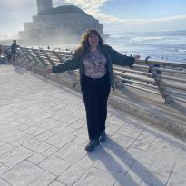 A woman standing in front of the Hassan II Mosque, next to the ocean