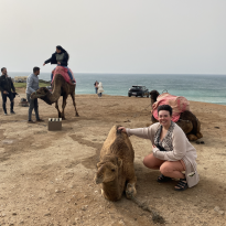 A woman petting a camel with the sea in the background