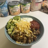 ground beef taco bowl with avocado, sour cream, cheddar cheese, and taco sauce over quinoa 