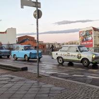 Three Trabi cars in street, two blue on the left and one white one on the right that says E-Force 1