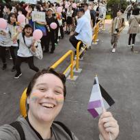 Author, Macks, smiling in front of Tokyo Pride Parade with the asexual pride flag.