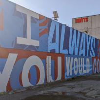 Large mural in white, blue, and red saying "I Always Knew You Would Come Back"