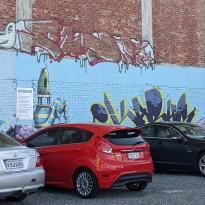 A mural of some shapes and a human-like bird on the wall of a parking lot 