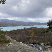 Blue lake, rocky path, green vegetation, rolling hill, and gray clouds