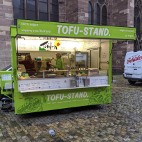 Lime green food stand with silhouettes of leaves on it that says Tofu-Stand 
