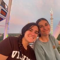 Two girls together on a ferris wheel smiling at sunset