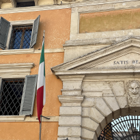 In front of a building's gate stands a statue and an Italian flag