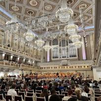 A beautiful neoclassical concert hall with ornate, painted figures on the ceiling, chandeliers, and orchestra instruments at the front of the hall