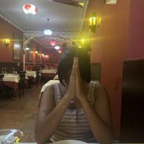 An image of me at a table in the Indian restaurant with my hands folded in prayer waiting for our food to arrive.