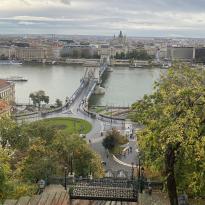 A heightened view of Budapest Parliament, and the roads stretching across a bridge into another district. At the bottom of the photo, it shows the rails of the cable car that brought the photographer to the vantage point.