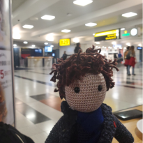 A doll resembling Sherlock from the BBC series "Sherlock" staring at the camera in the middle of the airport in a restaurant.