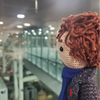 A doll resembling Sherlock from the BBC series "Sherlock staring out the airport window wistfully.