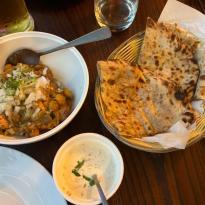 In this photo there is paratha which is a flatbread that is fried in a pan and samosa chaat which is made with curry, chopped up samosa, and chutney.