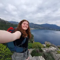 A ginger girl smiling into the camera with a scenic background behind her.