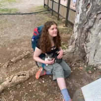 A cat sitting in the lap of a ginger girl who is in the middle of a conversation. She is not paying attention to the conversation because there is a cat in her lap. Obviously.