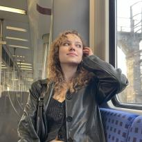 A college-aged girl sitting on a train wearing a black leather jacket, top, and skirt.