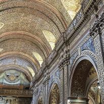 An interior image of an ornate, arched church ceiling. Intricate gold across the ceiling.