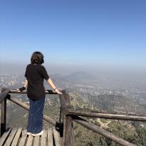Student looking out at a view of Santiago from a wooden platform at a viewpoint on the Cerro El Carbón trail