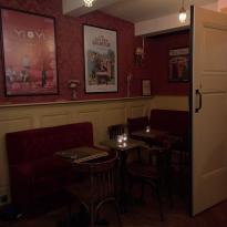 A table crammed into the corner of a low-lit bar. The table has two seats and is paired with movie posted plastered onto the neighboring wall.