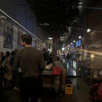 A crowded and busy hallway bustling with people as they order at the bar and sit at various tables.