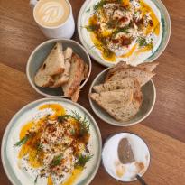 Two plates of turkish eggs (a dish where poached eggs are served on a bed of yogurt with spices and dill), two lattes, and two small bowls of bread