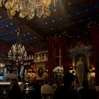The ornate, dark interior of Cafe de Las Horas. A bright chandelier is visible in the upper left and people are seen talking around small tables.