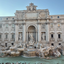 The Trevi Fountain in the evening from a second floor store window with crowds of toursits gathered around the edge of the fountain.