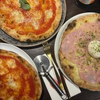 Three pizzas on plates at a dinner table.