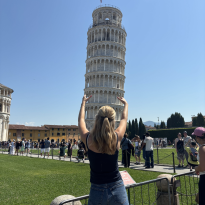 The Leaning Tower of Pisa with a girl posing in front as if she is holding up the leaning tower.