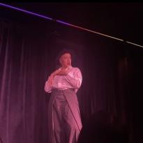 A drag performer in a black and white suit under pink lighting.