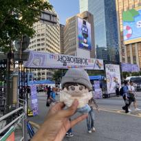 A hand holding up a plush doll in front of the entrance to the Seoul Queer Culture Festival.