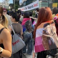 Festival attendees carrying lesbian pride flags with banners that read "Homosexuality is sin! Return to Jesus!" and "Homo sex is sin! Repent!" in the background.