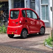 A 4-wheeled parked red vehicle that only hosts 2 people. 