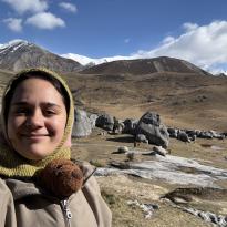 A photo of Pono in a windbreaker and balaclava and Teddy bear with the rocky dry landscape of Kura Tāwhiti behind.
