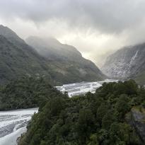 A massive landscape of mountains and valleys with small rivers running through and the sun peaking through the clouds.