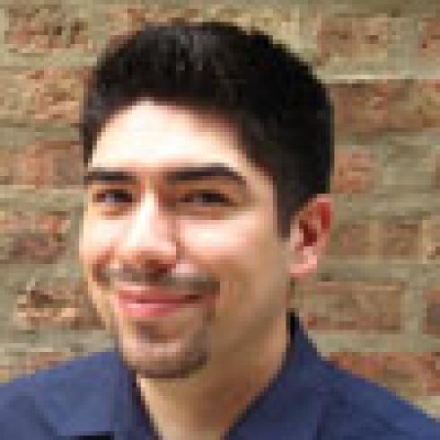 Smiling person with short dark hair and a goatee, in front of a brick wall. This alt text was added with Al; accuracy may vary.