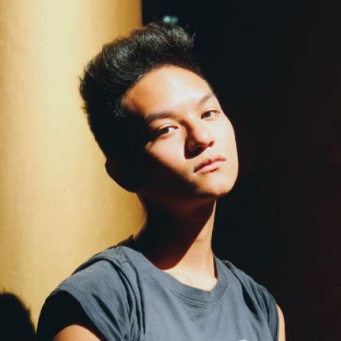 Young person in shadow with contemplative expression, sunlight on face. This alt text was added with Al; accuracy may vary.