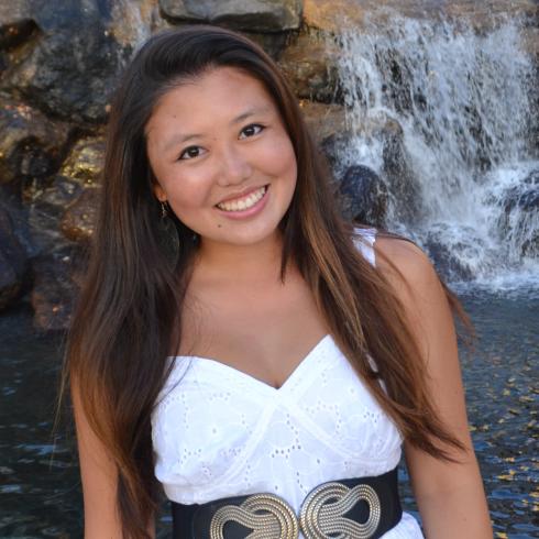 Smiling woman in a white dress stands by a waterfall. This alt text was added with Al; accuracy may vary.