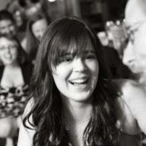 Smiling woman by a tree, wearing a beige sweater and feather earring. This alt text was added with Al; accuracy may vary.